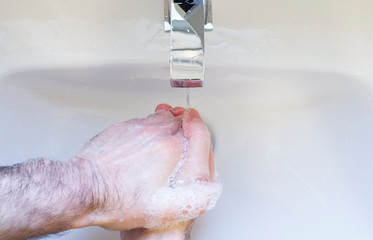 Fototapeta premium Soapy wet hands washing with blue anti-bacterial soap under tap