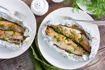 Oven baked whole pollock in foil in the oven, served on a white plate, selective focus