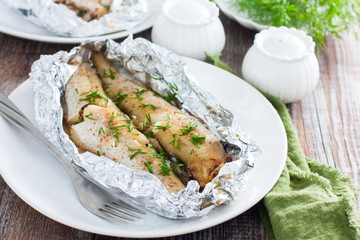 Oven baked whole pollock in foil in the oven, served on a white plate, selective focus