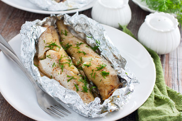 Oven baked whole pollock in foil in the oven, served on a white plate, selective focus