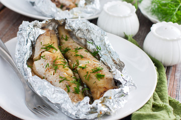 Oven baked whole pollock in foil in the oven, served on a white plate, selective focus