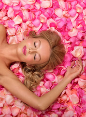 Beautiful slim young woman lying on petals of pink roses. Perfect figure.