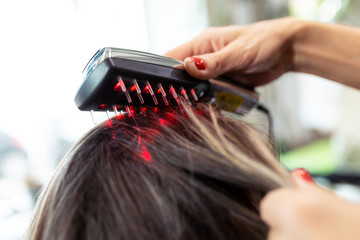 Hairdresser doing a treatment with ultrasonic and infrared laser comb for hair regrowth in her woman client at the salon.