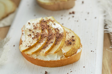 White bread with soft cheese, pieces of pear sprinkled with chocolate on a white wooden table. Healthy Breakfast concept.