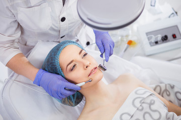 Cosmetology. Beautiful Woman At Spa Clinic Receiving Stimulating Electric Facial Treatment From Therapist. Closeup Of Young Female Face During Microcurrent Therapy.