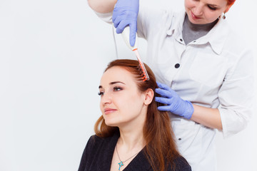 A young woman visited a dermatologist. Receiving electric darsonval facial massage procedure at beauty salon. White background