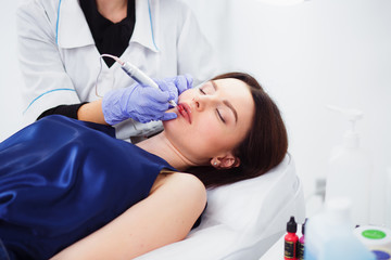 Naklejka premium Young woman having permanent makeup on lips in beautician salon on a white background. Close up
