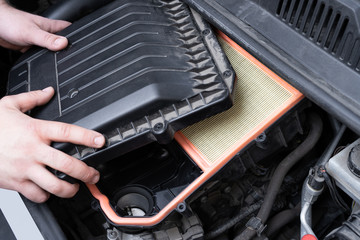 Caucasian man assembilng air box with new filter in car engine bay. Mechanic repair or vehicle...