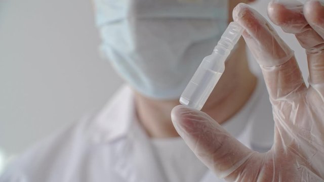 Hand in medical glove showing plastic ampoule with antiviral vaccine. Close up ampoule with liquid medicine in doctor hand in protective glove. Stop corona virus concept