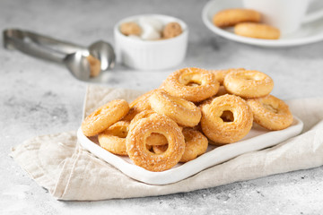Puff pastry sprinkled with sugar in a white plate on a light gray background. Cookies sprinkled with sugar. Sweet pastries