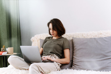Fototapeta na wymiar Young female using laptop, communicates on internet with customer in home on sofa. Cozy home office workplace, remote work, E learning concept on quarantine and self-isolation