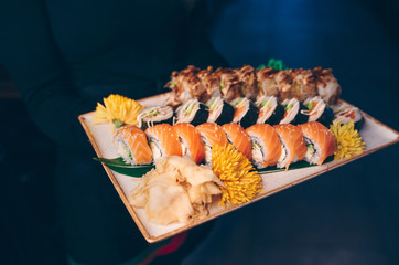 Close-up Hand Waiter holding Set Delicious fresh Sushi slate plate, Japanese raw fish   in traditional restaurant. Philadelphia flesh Rolls served on plate in sushi bar.  Japan food menu service
