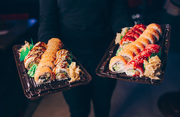 Close-up Hand Waiter holding Set Delicious fresh Sushi slate plate, Japanese raw fish   in traditional restaurant. Philadelphia flesh Rolls served on plate in sushi bar.  Japan food menu service