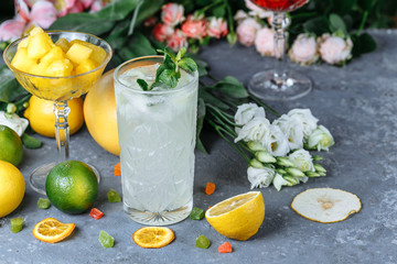 Summer fresh cold drink beverages. Ice Lemonade in the jug and lemons and orange with mint on the table outdoor. Orange lemonade in a glass