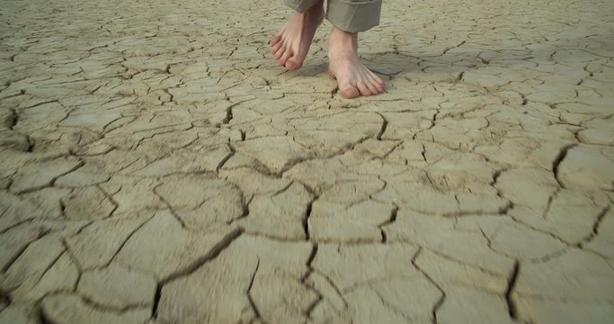 A young man walks barefoot on dry, cracked ground . Slow-motion close-up.