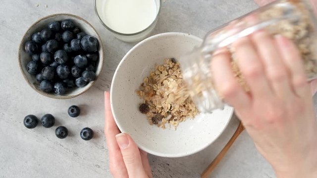 Woman pouring healthy breakfast cereals in bowl. Oat muesli with nuts and dried fruits. Clean eating, dieting, fitness menu concept