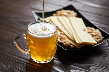 Mug of unfiltered light wheat beer with beer snacks on wooden table