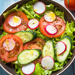 A very simple salad with fresh cucumbers, radishes, tomatoes and lettuce, olive oil and ground pepper - homemade summer European salad, top view