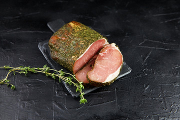 Gerky pork with spices, fresh green thyme, slate cutting board on black stone table. Polendwitz is a jerky tenderloin