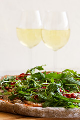 Pizza on rye pastry with ramiro pepper, arugula and parmesan. Pizza served on a wooden board with white wine.