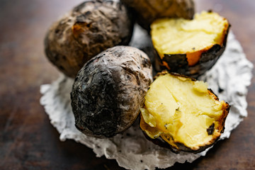 Baked in the fire potatoes in the skin according to the village recipe and method, directly in the ashes. Charred, fragrant tubers, a hot dish on a white stone plate