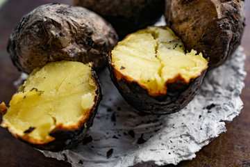 Baked in the fire potatoes in the skin according to the village recipe and method, directly in the ashes. Charred, fragrant tubers, a hot dish on a white stone plate