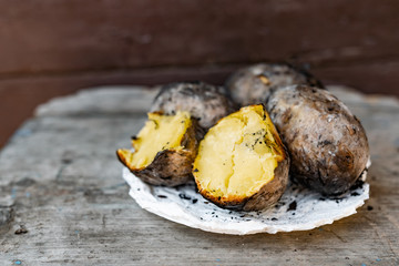 Baked in the fire potatoes in the skin according to the village recipe and method, directly in the ashes. Charred, fragrant tubers, a hot dish on a white stone plate