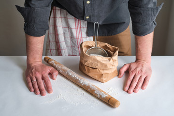 Man holds a bag of flour in his hands. Flour sieve and rolling-pin. Preparing the dough for baking. Making homemade cuisine for family. Chef in the kitchen cooking pastry. Healthy delicious culinary