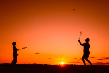 Plakat Father and son playing badminton in the evening, silhouettes of people exercising in nature, recreation, sport, lifestyle concept 