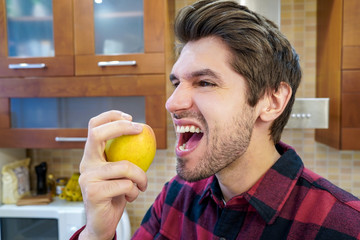 Portrait of a young attractive male chef biting an apple in the kitchen wearing a shirt 