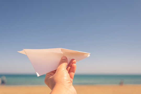 A girl is launching a paper airplane on the sunset beach. Travel and summer concept.