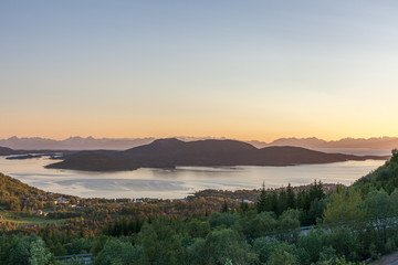 A mystical fjord in Norway with mountains and fog hanging over the water in polar day. midnight sun, selective focus