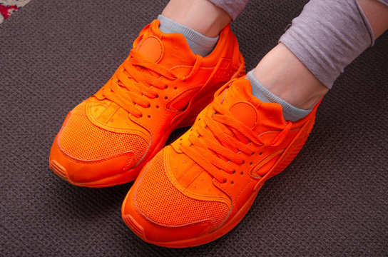 Female legs in gray sweatpants, leggings in bright orange sneakers for sports, jogging, fitness with high soles on gray Karimat. Female legs in orange sneakers on a gray mat for yoga, sports,  tourism