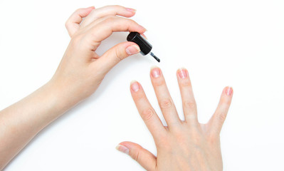 Manicure at home, during quarantine. Home manicure. The girl applies a transparent varnish, cuticle oil, nails on a white background with a brush on the nail.  Macro