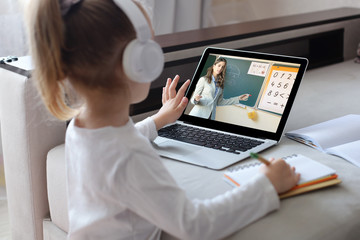 Distance learning. Cheerful little girl girl in headphones using laptop studying through online...