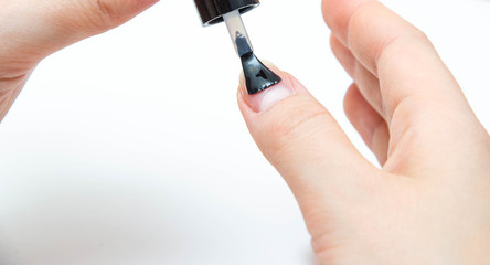 Manicure at home, during quarantine. Home manicure. The girl applies a transparent varnish, cuticle oil, nails on a white background with a brush on the nail.  Macro