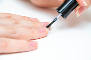 Manicure at home, during quarantine. Home manicure. The girl applies a transparent varnish, cuticle oil, nails on a white background with a brush on the nail.  Macro