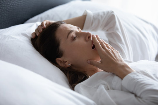 Close up woman woke up lying in bed yawn feels tired after night sleep need more rest or sleeping pills, new day to overloaded businesswoman, insomnia sleep disorder, alarm clock early morning concept