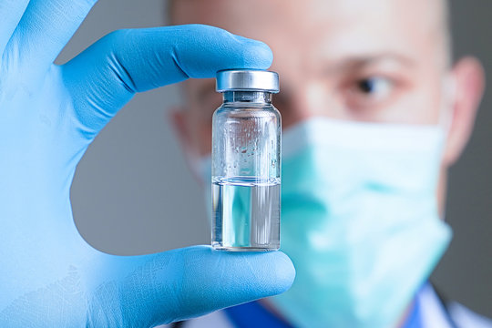 Close up hand of doctor in blue latex glove and medical gauze mask with glass ampoule. Health and vaccination concept