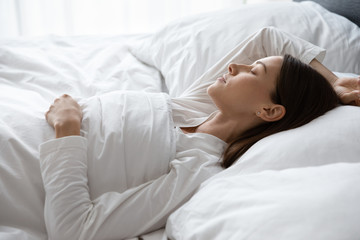 Close up view serene 30s woman sleeping covered with soft warm duvet lying on back in comfortable...