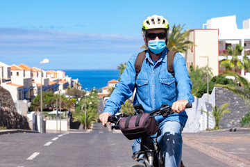 Portrait of a senior man on a bicycle with helmet and face mask. Phase two of the Covid-19 pandemic with partial end of the lockdown. Beautiful scenic background