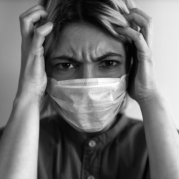 Close up image of stressful worried young woman wearing sterile medical mask holding hands on head, being paranoid because of coronavirus pandemic outbreak, does not want to listen to bad news