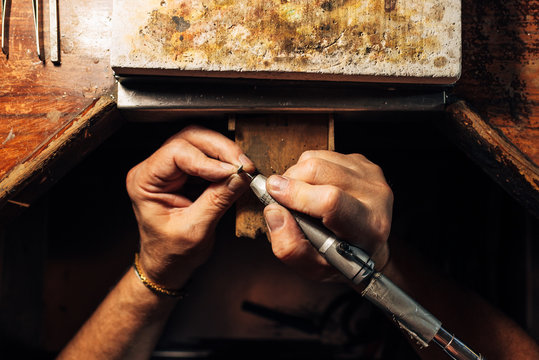The silver artist's hands work on a unique piece of jewelry. Zenith photograph of the artisan working in his workshop.