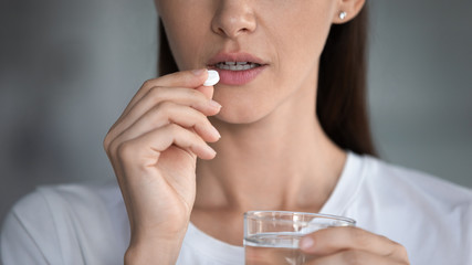 Close up female takes pill holds glass of water, minerals essential for women skin hair health,...