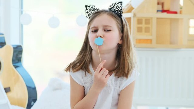 Cute little girl posing with paper lips on stick in kids room