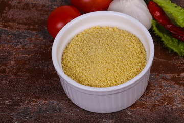 Raw couscous in the bowl served salad leaves, tomato and pepper