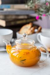 Sea-buckthorn tea in a glass teapot with white mugs on a light background. selective focus.