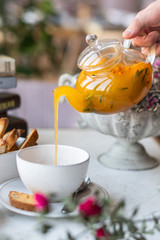 Sea-buckthorn tea in a glass teapot with white mugs on a light background. selective focus.