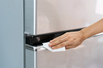 Hands of young Asian woman cleaning stainless steel refrigerator with wet wipe tissue at home