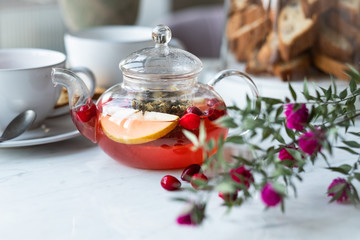 hot fruit tea with cranberries and apples in a glass teapot on a light background. selective focus.